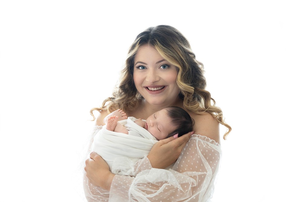 Mother cuddling swaddled newborn in white studio, capturing timeless Essex maternal love portrait